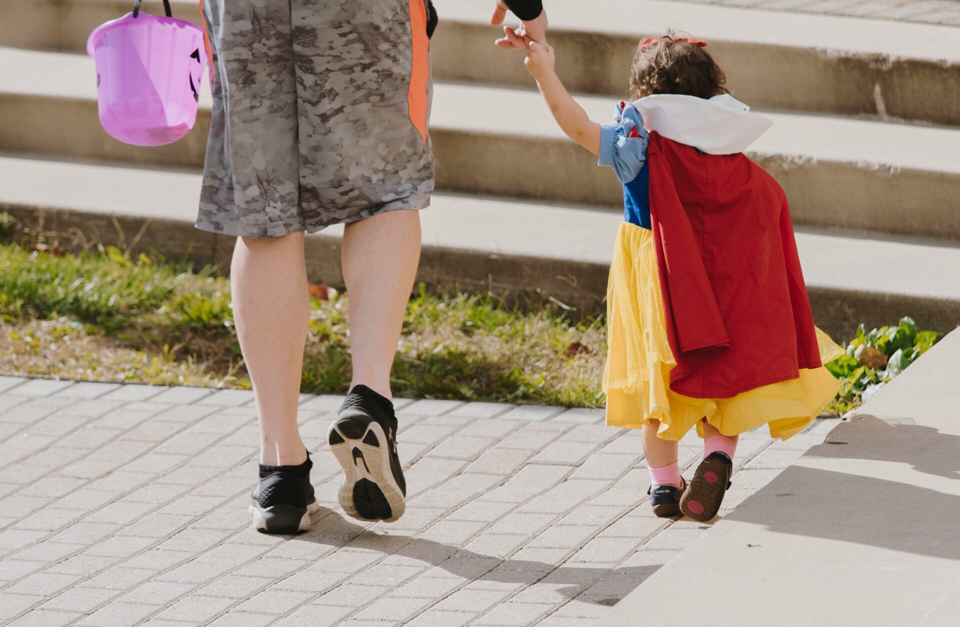 A parent holding a child's hand who is wearing a Halloween costume.