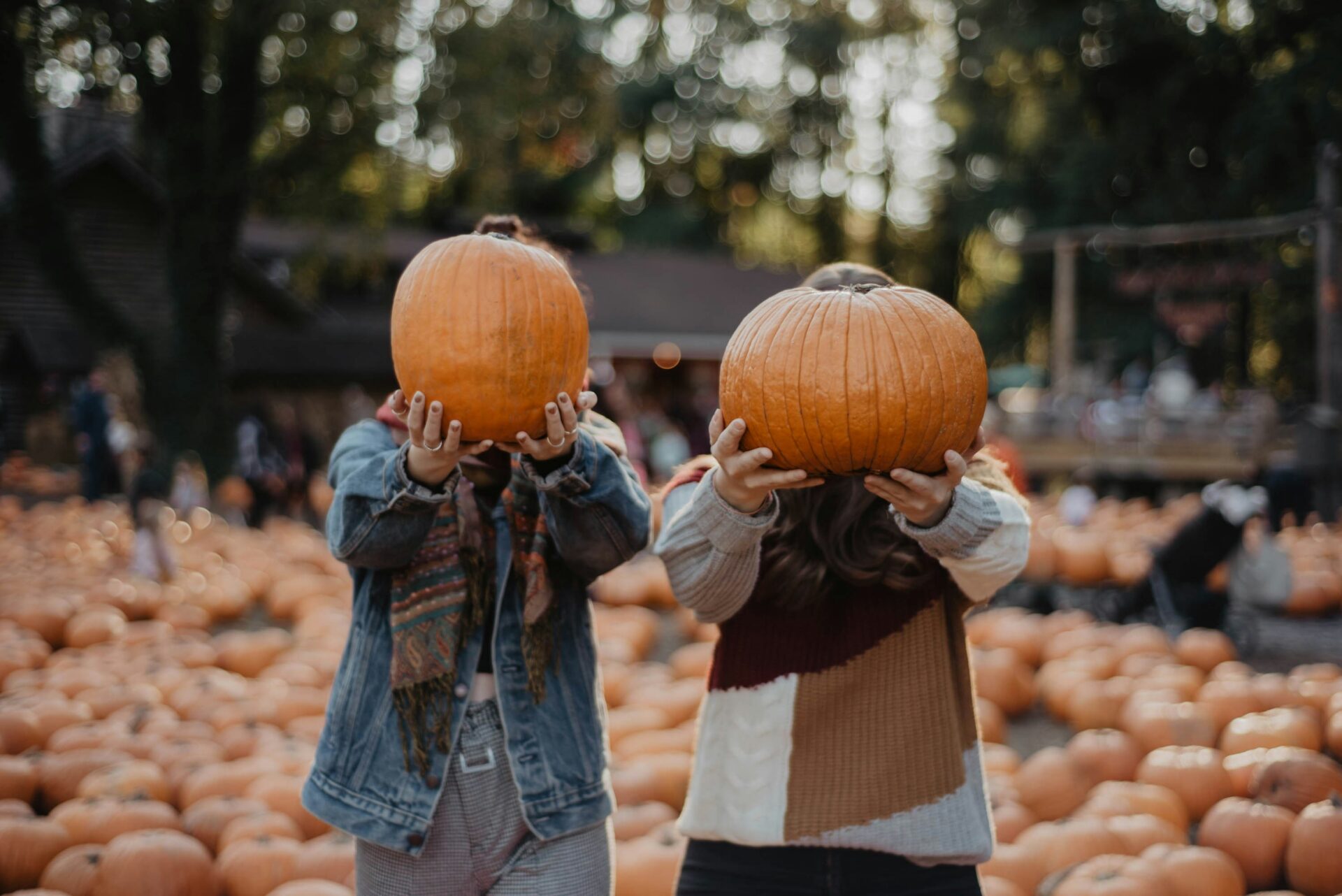Two women holding pumpkins in front of their face.